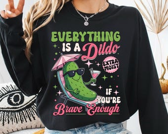 Può includere: Felpa nera con una grafica di un cetriolo con occhiali da sole, che si rilassa su una sedia a sdraio e tiene in mano un cocktail. Il testo recita "Everything is a Dildo if you're brave enough."