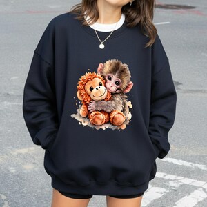 May include: Navy blue sweatshirt featuring a colorful illustration of two hugging monkeys. One monkey is brown and the other is orange. The graphic is centered on the front of the sweatshirt. The sweatshirt has a crew neck and long sleeves.