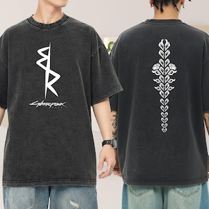 May include: Dark gray t-shirt with a white graphic on the front and back. The front features a stylized design with the word "Cyberpunk" underneath. The back displays a vertical floral-like design. The shirt has a vintage, washed look.