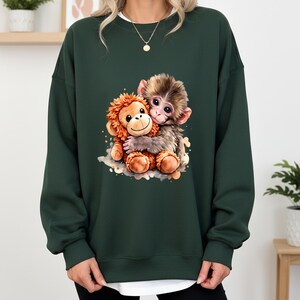 May include: Dark green sweatshirt featuring a graphic of two cartoon monkeys hugging. One monkey is brown and the other is orange. The sweatshirt has a crew neck and is made of a soft material.