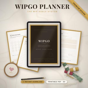 Op de afbeelding: Een Wipgo-planner-set met een donkere omslag met gouden accenten, meerdere witte planningspagina's, een ronde borduurring met een hartontwerp, een zwart potlood en verschillende kleine klossen gekleurd garen.