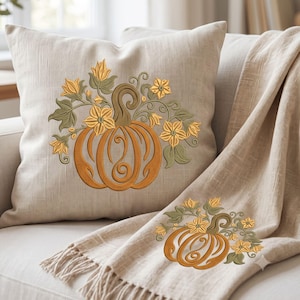 May include: A square beige throw pillow and a matching beige throw blanket with fringe, both featuring an embroidered design of an orange pumpkin with swirling vines and yellow flowers in a muted color palette on the front of each item.