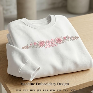 Op de afbeelding: Witte sweatshirt met een geborduurd bloemmotief. Het ontwerp toont roze rozen en een strik, met groene bladeren en stelen. De tekst "Machine Embroidery Design" staat onderaan de afbeelding.