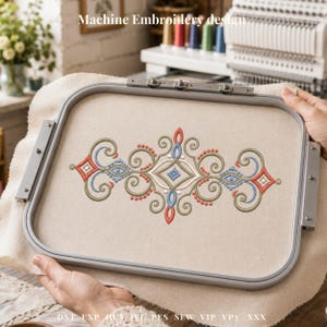 May include: A beige fabric stretched within a metal embroidery hoop, featuring a symmetrical design in red, blue, green, and beige thread. The design includes swirls, dots, and diamond shapes. Text at the top reads "Machine Embroidery design."