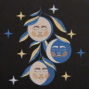 Puede incluir: Diseño celestial bordado con tres caras de luna con los ojos cerrados, rodeadas de hojas y estrellas doradas y azules sobre un fondo negro. Las lunas tienen caras beige con rubor melocotón y detalles azules y dorados. Las estrellas son doradas, azules y plateadas.
