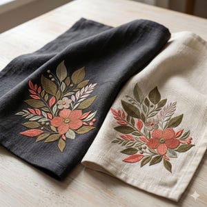 May include: Two rectangular kitchen towels, one in charcoal gray and one in off-white, each featuring an identical embroidered floral arrangement. The design includes coral-colored flowers, sage green leaves, and small berries in a botanical style.