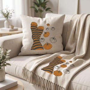 May include: A square throw cushion and a matching throw blanket in a light beige fabric. Both items feature a graphic print of two legs wearing orange and dark grey striped socks, surrounded by several orange and black-outlined pumpkin illustrations.