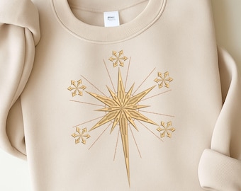 May include: A beige sweatshirt featuring a gold starburst design with six smaller star accents. The text "Embroidery design file Instant download" is at the bottom. The design is likely for embroidery projects.