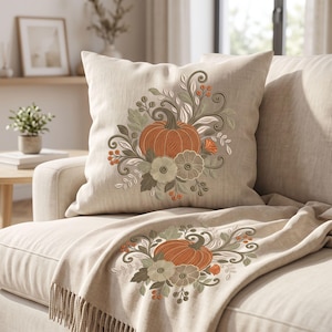 May include: A square throw pillow and a matching throw blanket in a light beige fabric. Both items feature an embroidered design of a central orange pumpkin surrounded by sage green leaves, swirling vines, and small orange berries.