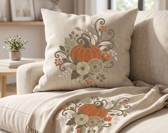 May include: A square throw cushion and a matching throw blanket in a light beige fabric. Both items feature an embroidered design of a central orange pumpkin surrounded by sage green leaves, swirling vines, and small orange berries.