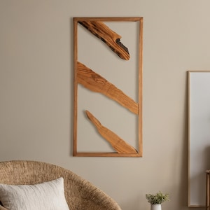 Puede incluir: Arte de pared de madera con un marco rectangular y tres elementos de madera diagonales. La madera muestra vetas naturales y tonos marrones. La obra de arte está montada en una pared neutra, ofreciendo un diseño moderno y minimalista.