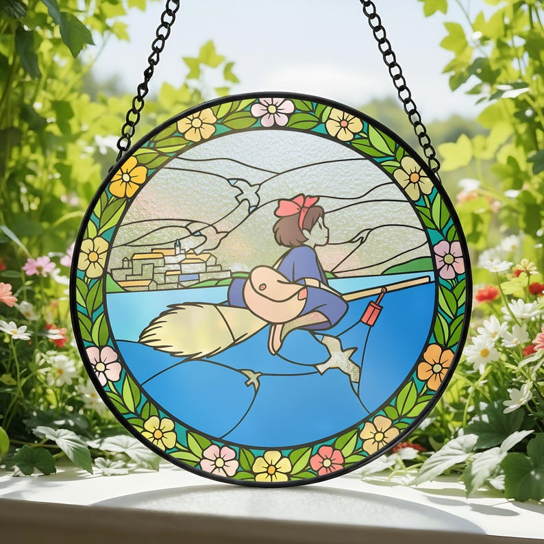 Puede incluir: Vidriera redonda que representa a una ni&ntilde;a de dibujos animados montada en una escoba sobre agua azul. La obra de arte tiene un marco de metal negro y una cadena para colgar. El borde est&aacute; decorado con flores coloridas y hojas verdes. Una pieza encantadora para cualquier habitaci&oacute;n.
