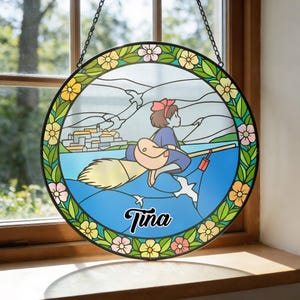 Puede incluir: Vidriera redonda que representa a una ni&ntilde;a de dibujos animados en una escoba sobre el agua, con un pueblo al fondo. El dise&ntilde;o est&aacute; enmarcado por un borde floral. El nombre "Tina" est&aacute; escrito en cursiva.