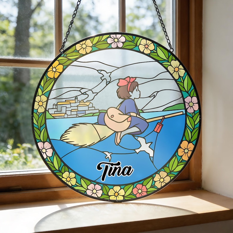 Puede incluir: Vidriera redonda que representa a una ni&ntilde;a de dibujos animados en una escoba sobre el agua, con un pueblo al fondo. El dise&ntilde;o est&aacute; enmarcado por un borde floral. El nombre "Tina" est&aacute; escrito en cursiva.