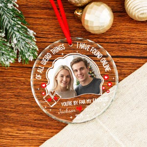 May include: A clear, round glass Christmas ornament with a red ribbon. The ornament features a photo of a couple and the text "OF ALL WEIRD THINGS I HAVE FOUND ONLINE, YOU'RE BY FAR MY FAVORITE." Includes a name and the year 2023.