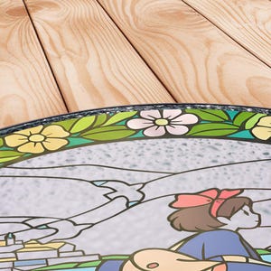 Puede incluir: Una bandeja redonda decorativa con un dise&ntilde;o de vidriera. La bandeja presenta un borde floral con flores amarillas y rosas y hojas verdes. El centro representa un personaje de dibujos animados con un vestido azul y un lazo rojo.