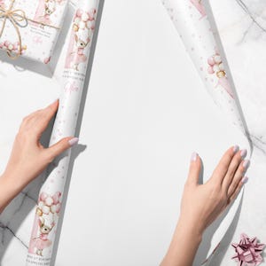 May include: Pink and white birthday wrapping paper featuring a cartoon bunny holding balloons. The paper has a repeating pattern of stars and the text "Happy 1st Birthday, a special niece" and the name "Olive".