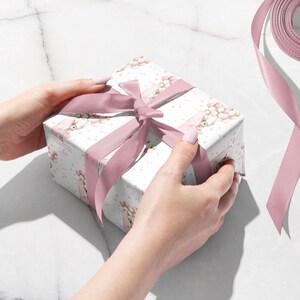 May include: A wrapped gift box with a pink satin ribbon tied in a bow. The gift wrap is white with a pattern of pink flowers and bunnies. The ribbon is a solid pink color.