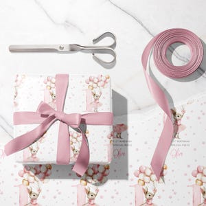 May include: A wrapped gift with a pink ribbon, scissors, and a roll of pink ribbon. The gift wrap features a bunny holding balloons, the number 1, and the text "Happy 1st Birthday Special Niece Olive".