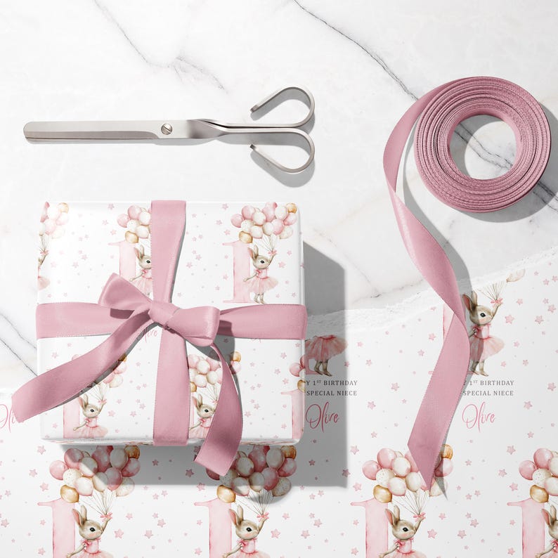 May include: A wrapped gift with a pink ribbon, scissors, and a roll of pink ribbon. The gift wrap features a bunny holding balloons, the number 1, and the text "Happy 1st Birthday Special Niece Olive".