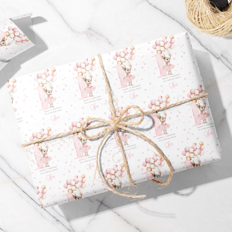 May include: White wrapping paper with a repeating pattern of a cartoon chihuahua wearing a pink tutu and holding balloons. The paper is tied with twine and features text that reads "Happy 1st Birthday to a Special Niece" and a name.