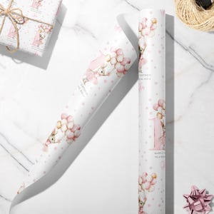 May include: White wrapping paper with a repeating pattern of a bunny holding balloons, pink stars, and the number 1. The text reads "Happy 1st Birthday to a Special Niece". A wrapped gift and a pink bow are also visible.