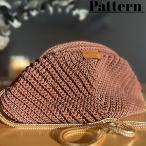 May include: A brown crocheted handbag with a gold chain strap. The bag features a ribbed texture and a small brown label. The words "Crochet Pattern" are in black text at the top of the image.