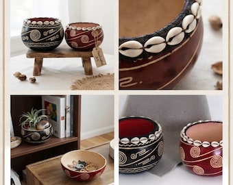 Könnte beinhalten: Zwei runde Schalen in Dunkelbraun und Rotbraun mit weißen Spiralmustern und Rändern, die mit weißen Kaurimuscheln verziert sind. Eine Schale enthält eine kleine Pflanze, die andere Schlüssel. Ein Etikett trägt die Aufschrift Handcrafted Art.