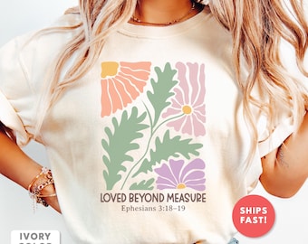 Könnte beinhalten: Elfenbeinfarbenes Sweatshirt mit einem floralen Design in Pastellfarben. Das Design umfasst rosa, lila und gelbe Blumen mit grünen Blättern. Der Text "LOVED BEYOND MEASURE" und "Epheser 3:18-19" ist unter der floralen Grafik aufgedruckt.
