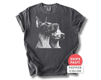 Può includere: T-shirt grigio scuro con grafica in bianco e nero di due cani. I cani sono rivolti verso destra, con la testa di uno appoggiata sull'altro. La maglietta ha maniche arrotolate e girocollo. Il testo "SHIPS FAST! PEPPER COLOR" è su un adesivo rosso e bianco.