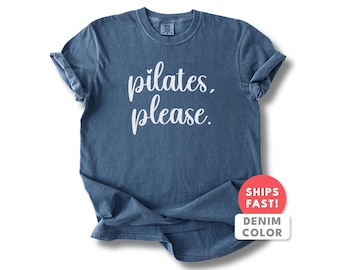 以下が含まれることがあります： 白い文字で「pilates, please」と書かれたデニムブルーのTシャツ。シャツはクルーネックで、袖がまくられています。赤と白のステッカーは、アイテムがデニムで、すぐに発送されることを示しています。