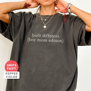 May include: Dark gray t-shirt with the text "built different (boy mom edition)" in white. The shirt has a relaxed fit and a crew neck. The shirt is a solid color and has short sleeves.