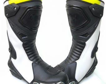 Botas de motociclista de cuero blanco y negro, equipo de pista blindado, detalles en amarillo de alta visibilidad.