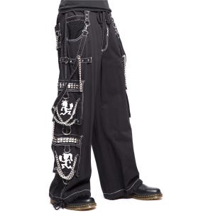 May include: Black cargo pants with white stitching, multiple pockets, and silver chains. The pants feature a white graphic on the pockets and are styled with black boots. The pants have a wide leg design.