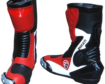 May include: Pair of red, black, and white motorcycle boots. The boots have a high-top design with a red shin guard and a black upper. The Ducati logo is visible on the side. The boots have a silver toe slider and are designed for protection and performance.