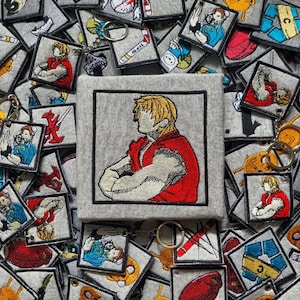 Może przedstawiać: Kwadratowa naszywka z szarej tkaniny z wyhaftowaną ilustracją blond postaci w czerwonym gi bez rękawów ze skrzyżowanymi ramionami. Naszywka otoczona jest kolekcją podobnych kwadratowych naszywek z różnymi wzorami postaci.
