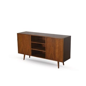 Op de afbeelding: Een houten kast in mid-century modern stijl met een donkerbruine afwerking. De kast heeft twee deuren en een open schapgedeelte met twee planken. Hij staat op vier taps toelopende poten.