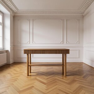 Könnte beinhalten: Ein hellbrauner Holzkonsolentisch mit einer Lamellenfront und einem unteren Regal. Der Tisch hat vier runde Beine und steht vor einer weißen Wand mit dekorativen Leisten. Der Raum hat einen Parkettboden.
