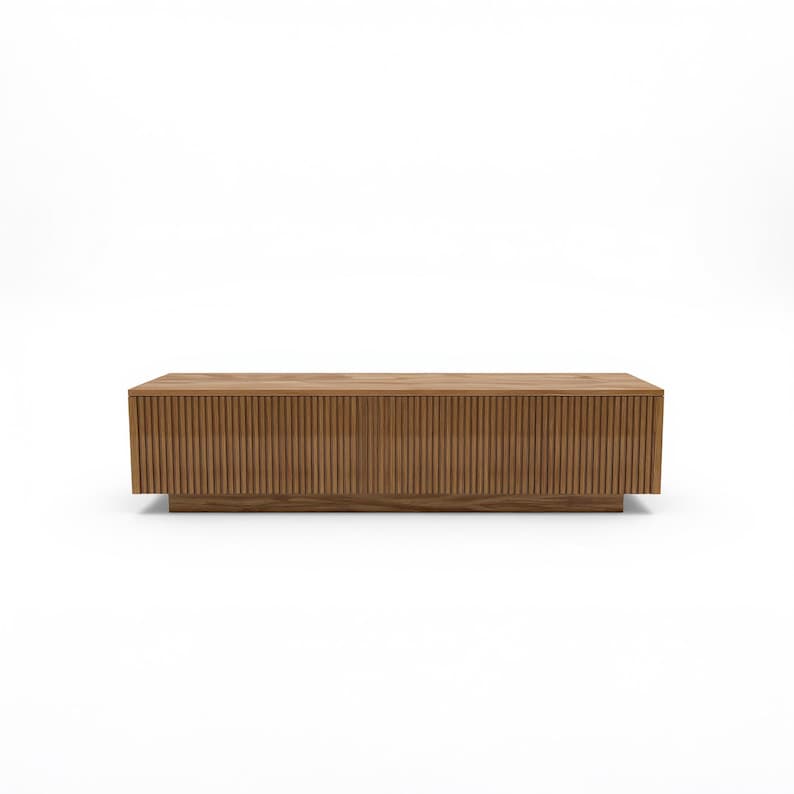 May include: A rectangular wooden coffee table with a light brown finish. The table features vertical grooved detailing across the front and sides, and sits on a low, solid base. The design is modern and minimalist.