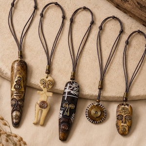 May include: Five pendants on dark brown cord necklaces. The pendants feature carved bone and dark wood shapes, including elongated masks and a circular disc, accented with brass wire spirals and metal coils at the top of each piece.