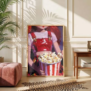 May include: A framed art print depicts a person holding a large popcorn bucket. The person wears a red overall and a white shirt. The popcorn bucket is red and white striped. The art has a warm color palette and is displayed in a room with a pink ottoman and a leopard print rug.