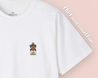 Puede incluir: Camiseta blanca con un pequeño gráfico de murciélago y el texto "JUST HANGIN'". La camiseta también presenta el texto "The Emotional Zoo" en una fuente diagonal. El gráfico del murciélago es marrón y beige.