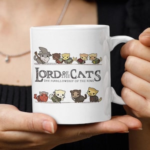 Könnte beinhalten: Weiße Keramik-Tasse mit dem Text "Lord of the Cats" und Cartoon-Katzen-Illustrationen. Die Tasse hat einen Henkel. Das Design umfasst verschiedene Katzen in verschiedenen Posen.