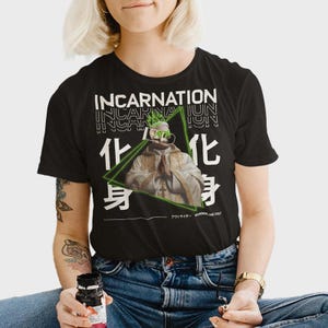 Könnte beinhalten: Schwarzes T-Shirt mit dem Wort "INCARNATION" in Weiß, vertikal wiederholt. Eine Grafik einer Statue mit einem grünen Dreieck und japanischen Schriftzeichen ist zentriert. Der Text "WANDERING CULT" befindet sich unten.