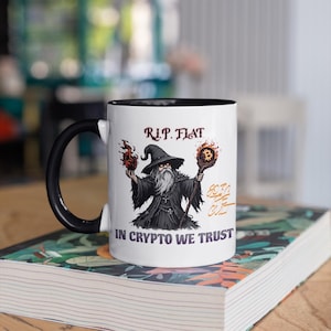 May include: White ceramic mug with a black handle and interior. The mug features a wizard graphic holding fire and a Bitcoin staff, with the text "R.I.P. Fiat" and "In Crypto We Trust".