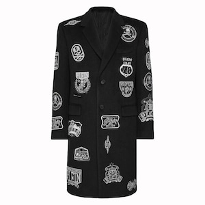 May include: Black wool coat with multiple white and black patches. The patches feature skull and crossbones, crests, and the word "PLEIN". The coat has a classic design with a notched collar and button closure.