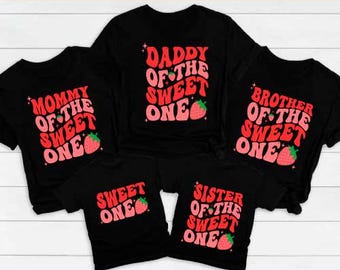 Puede incluir: Un conjunto de camisetas negras con las frases "Mommy of the Sweet One", "Daddy of the Sweet One", "Brother of the Sweet One", "Sweet One" y "Sister of the Sweet One" en rojo y rosa, con fresas.