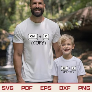 以下が含まれることがあります： 黒い文字が入った白いTシャツ2枚。1枚のシャツには「Ctrl + C (COPY)」と書かれており、もう1枚には「Ctrl + V (PASTE)」と書かれています。シャツは男性と子供が着用しています。背景はぼやけた屋外のシーンです。