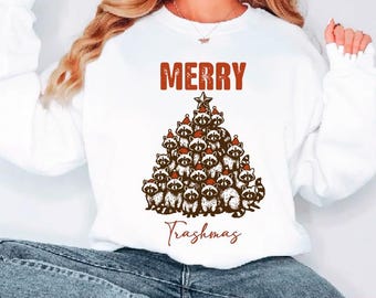 May include: White sweatshirt featuring a Christmas tree design composed of raccoons in Santa hats. The word "MERRY" is above the tree, with "Trashmas" below. The graphic is in brown and red tones, perfect for the festive season.