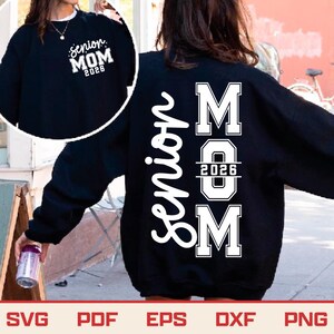May include: Black sweatshirt with white text that reads "Senior MOM 2026" on the back and front. The front has a smaller design. The sweatshirt is a crew neck style. The bottom of the image has the words "SVG PDF EPS DXF PNG".
